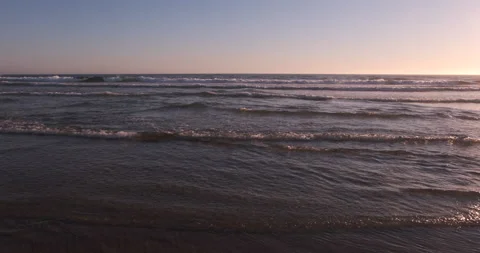 Shallow waves rushing towards camera on wide flat beach at sunset Stock Footage 135363792