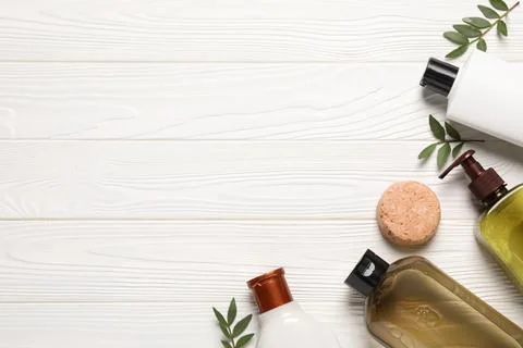 Shampoo bottles, leaves and solid shampoo bar on white wooden table, flat l.. Stock Photos