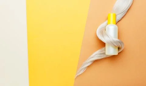 Shampoo orange bottle with lock curl of blonde hair. Hair hygiene treatment c Stock Photos