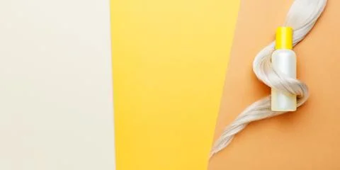 Shampoo orange bottle with lock curl of blonde hair. Hair hygiene treatment c Stock Photos