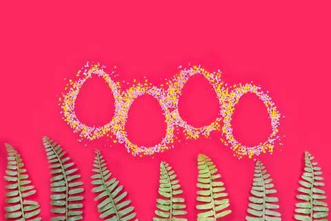 Shape of easter eggs and color sugar sprinkle and green fern leaveson red Stock Photos