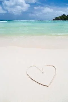 The shape of a heart in the sand of a clean white beach with turquoise water Stock Photos