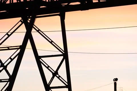 The shape or silhouette of a tower crane against the sky and the setting sun. Stock Photos