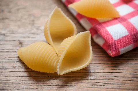 Shaped shell pasta and red napkin on wooden background Stock Photos