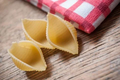 Shaped shell pasta and red napkin on wooden background Stock Photos