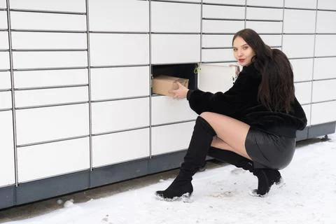 The shapely student crouched next to the parcel locker and holds a gray parcel 스톡 사진