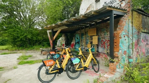 Shared electric yellow bikes parked under a roof beside a graffiti-covered Stock Footage 340935132