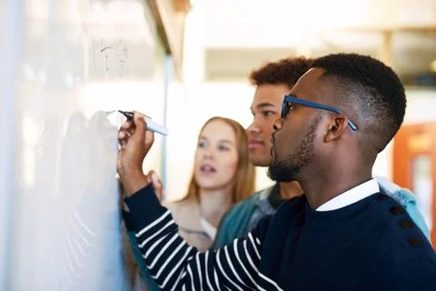 Sharing his method with the group. a young man writing on a whiteboard while Stock Photos