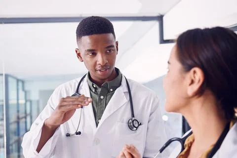 Sharing medical knowledge. two young doctors discussing working while standing Stock Photos