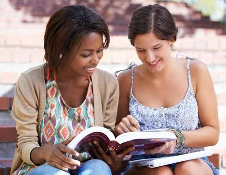 Sharing their knowledge. Two friends studying in the park on the steps together. Stock Photos
