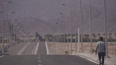 SHARM EL SHEIKH, EGYPT - MARCH 7:Lonely man walking on the road near mountains Stock Footage 74917682