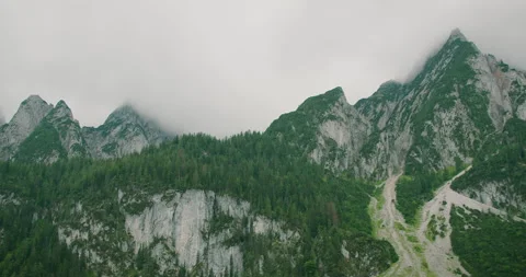 Sharp alpine peaks surrounded by dense forests under a cloudy sky, evoking a Stock Footage 307116346