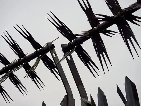 Sharp, angled barbed security fence silhouetted against a cloudy sky. Stock Photos