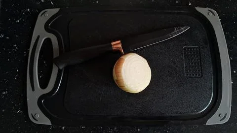 Sharp black kitchen knife resting beside a fresh sliced yellow onion Stock Photos