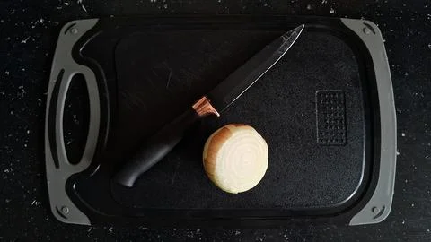 Sharp black kitchen knife resting beside a halved yellow onion Stock Photos
