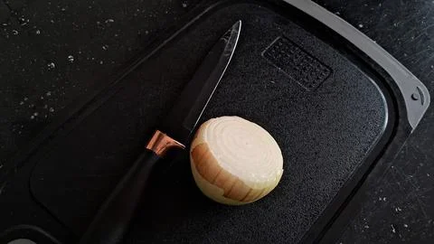 Sharp black kitchen knife resting beside a halved yellow onion Stock Photos