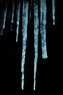 Sharp blue icicles hanging down against a dark night sky in winter Stock Photos
