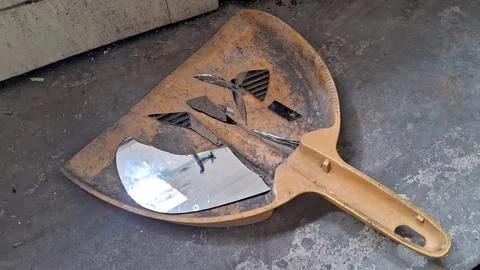 Sharp broken mirror shards resting inside a worn yellow dustpan tool Stock Photos
