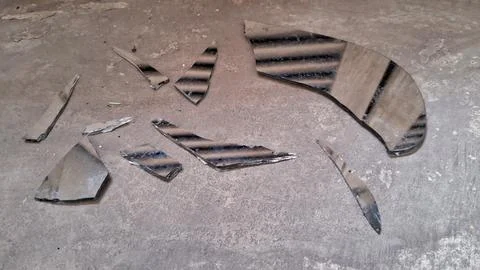 Sharp broken mirror shards scattered across a rough concrete floor surface Stock Photos