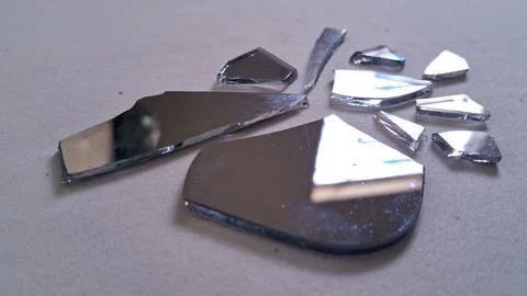 Sharp broken mirror shards scattered on a smooth grey surface Stock Photos