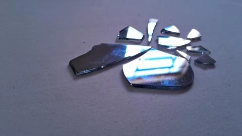 Sharp broken mirror shards scattered on a smooth grey surface Stock Photos
