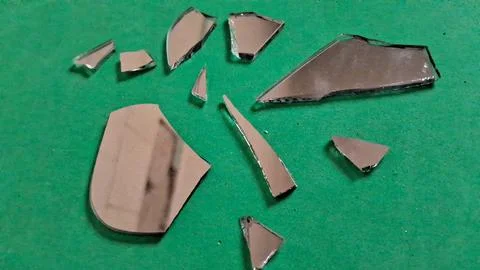 Sharp broken mirror shards scattered across a vibrant green textured surface Stockfoto's