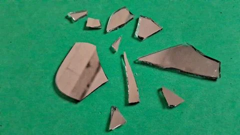 Sharp broken mirror shards scattered across a vibrant green textured surface Stockfoto's