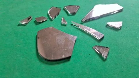Sharp broken mirror shards scattered on a bright green flat surface Stockfoto's