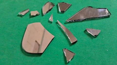Sharp broken mirror shards scattered across a vibrant green textured surface Stockfoto's