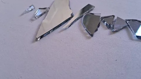 Sharp broken pieces of a silver mirror on white surface Stock Photos
