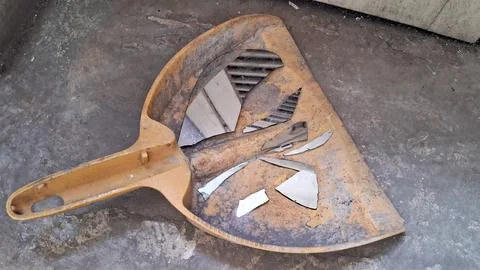 Sharp broken shards of glass resting inside a dirty yellow dustpan Stock Photos