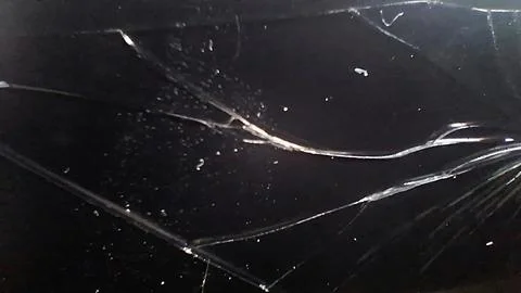 Sharp cracks spreading across a dark black shattered glass screen surface Foto stock