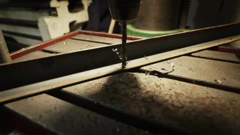 A sharp drill bit penetrates a metal bar, creating steel shavings in a gritty Stock Footage 332130338