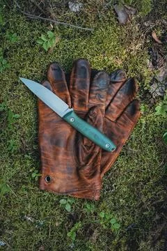 A sharp fixed blade knife with a green handle lying on brown leather work glo Stock Photos