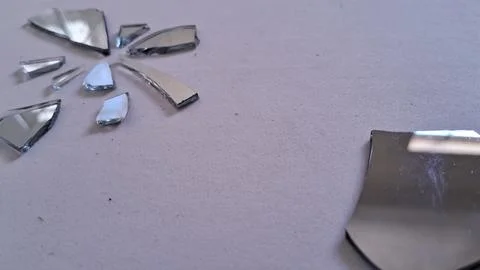 Sharp fragments of a shattered mirror lying on textured paper surface Stock Photos