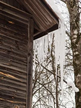 Sharp, frozen icicles hang on the corner of the roof, winter or spring. Foto stock
