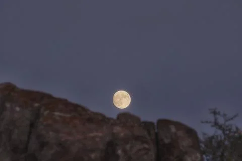 A sharp full moon shines in the dark twilight sky above a blurred rocky ridge Stockfoto's