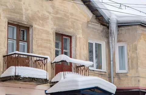 Sharp ice icicles hang from the drainpipe at the edge of the roof. Stock Photos