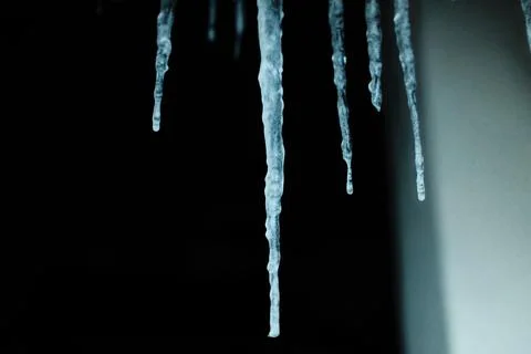 Sharp icicles hanging against a dark background during winter evening Stock Photos