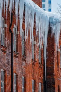 Sharp icicles hanging from the roof of a brick building create a striking yet Stock Photos