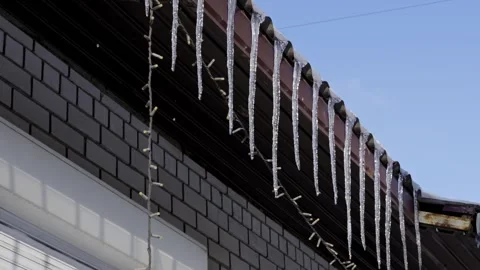 Sharp Icicles Hanging From a Rooftop Gutter on a Sunny Winter Day Stock Footage 325881013