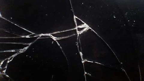 Sharp jagged cracks spreading across a dark black glass surface Stock Photos
