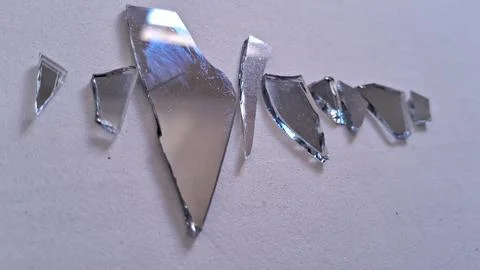 Sharp jagged pieces of broken mirror scattered on white textured surface Stock Photos