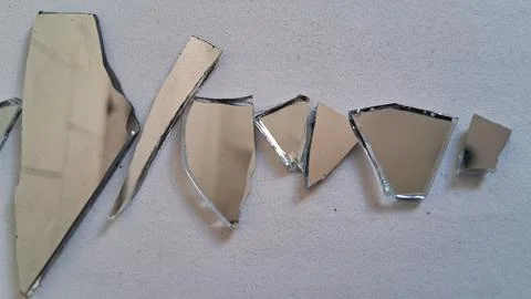 Sharp jagged pieces of broken mirror reflecting light on textured surface Stock Photos