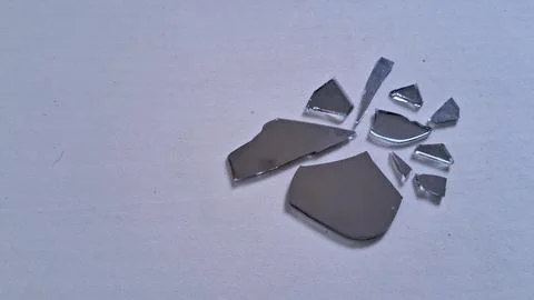 Sharp jagged pieces of broken mirror scattered on white surface Stock Photos