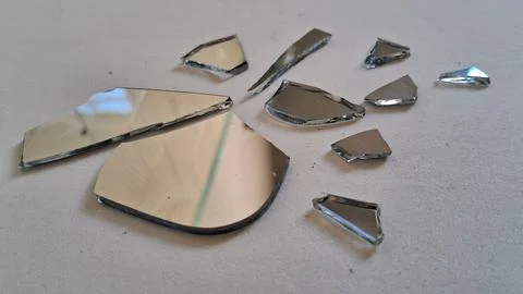 Sharp jagged pieces of broken mirror scattered across white surface Stock Photos
