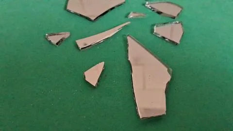 Sharp jagged pieces of broken mirror scattered on green background Stockfoto's