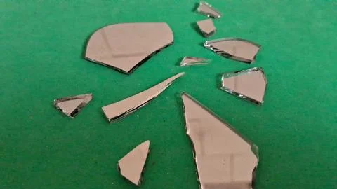 Sharp jagged pieces of broken mirror reflecting light on green background Stockfoto's