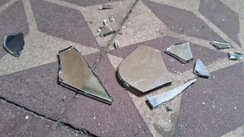 Sharp jagged pieces of a shattered mirror lying on tiled floor Stock Photos