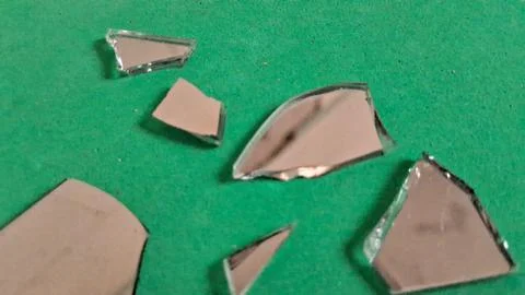 Sharp jagged shards of broken mirror resting on green paper Stockfoto's
